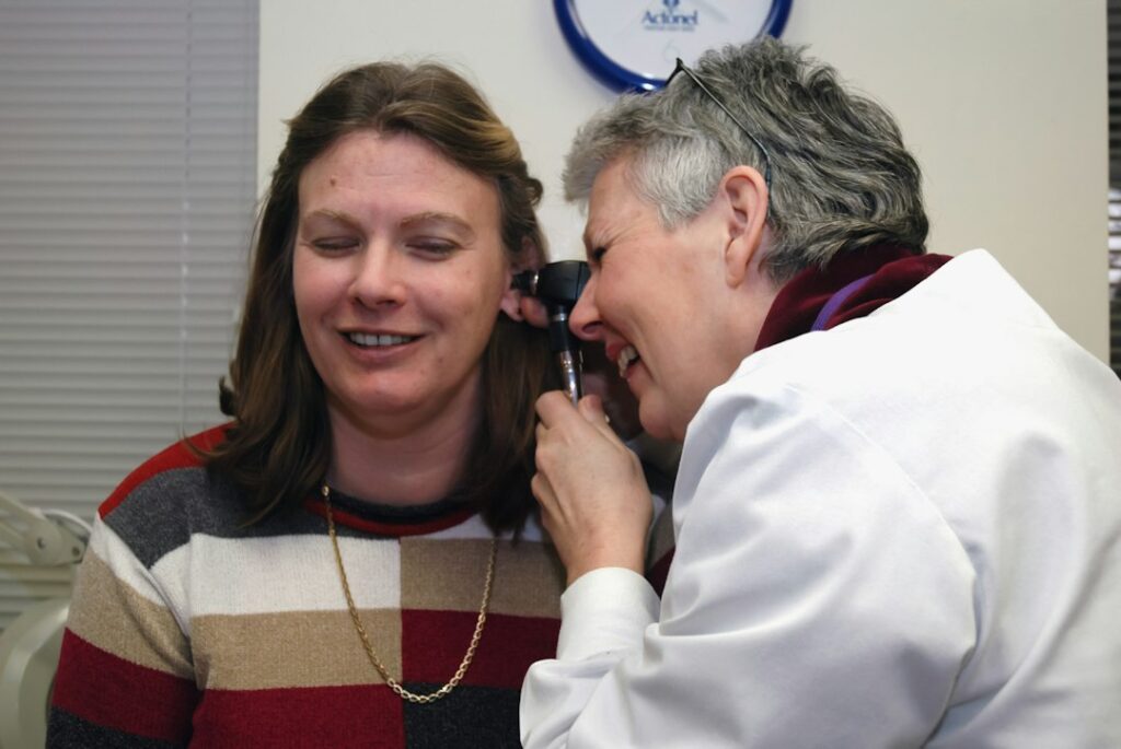 Person applying lubricating eye drops beside a window with a humidifier in the background.
