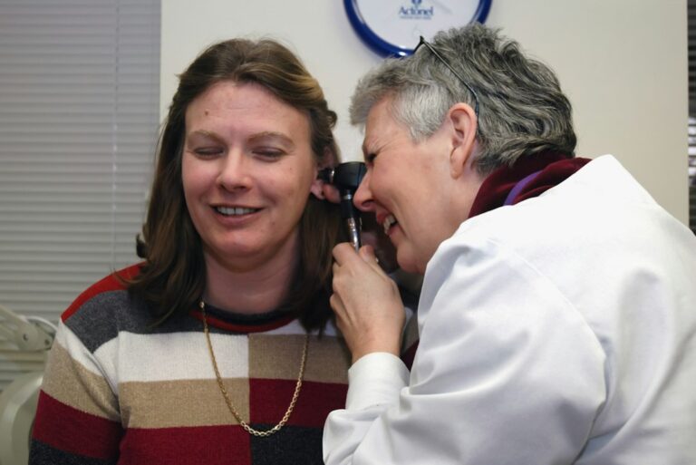 Person applying lubricating eye drops beside a window with a humidifier in the background.